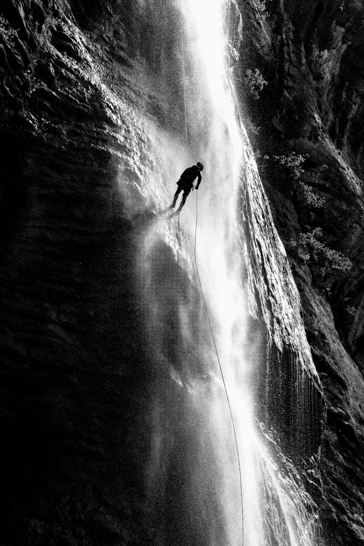 Canyoniste descendant en rappel le long d'une cascade, en noir et blanc